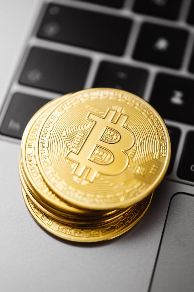 finance your home with crypto, Close-up of golden Bitcoin coins stacked on a laptop keyboard showcasing cryptocurrency and finance concepts.
