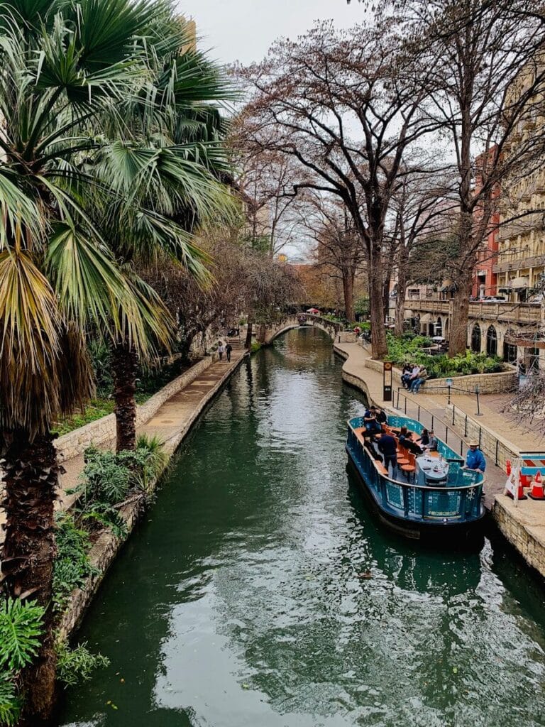San Antonio Riverwalk boat on river between trees during daytime