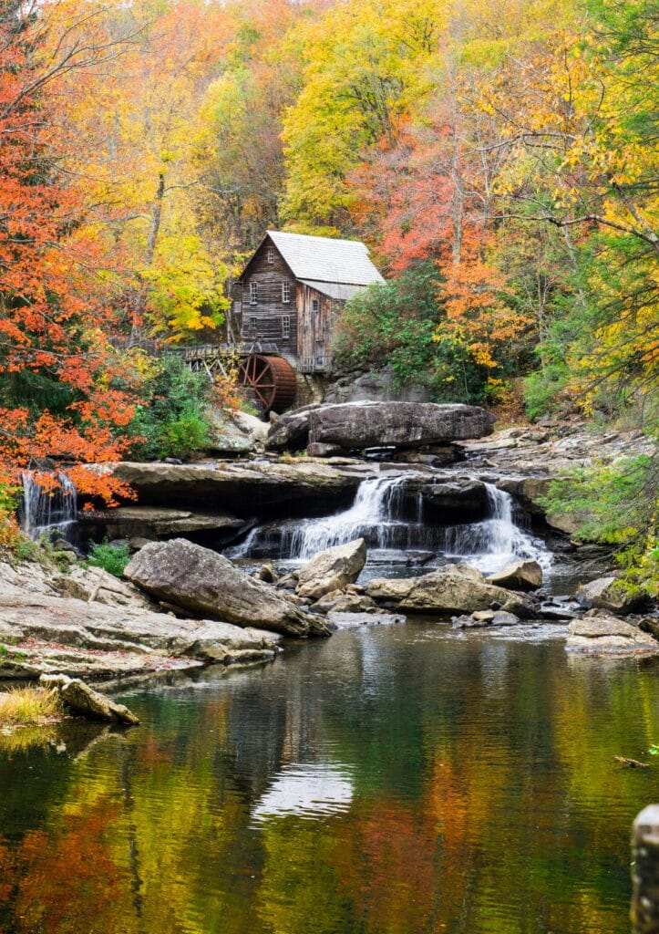 Idyllic scene of a gristmill surrounded by colorful autumn trees, reflecting in a serene creek. West Virginia real estate 