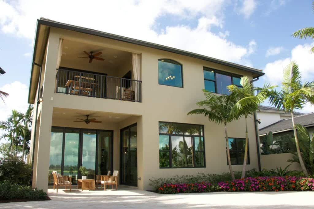 A modern two-story home with a balcony, patio, and lush garden.