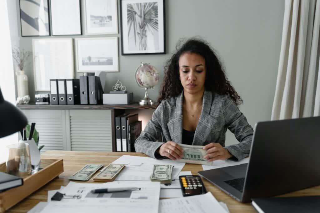 Focused woman counts cash at desk surrounded by office items, emphasizing finance and professionalism. Real Estate Commissions.