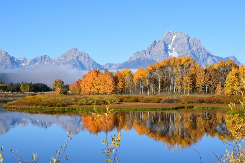 Breathtaking autumn scene of Grand Teton reflecting in a serene lake in Wyoming, USA.