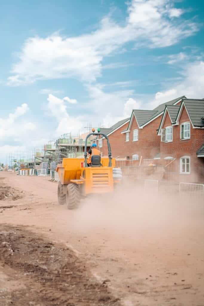 New home community has a large yellow tractor driving down a dirt road